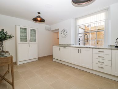 A kitchen with white cabinets a large window with a view outside a clock on the wall and a glass cabinet at 23 Daniel Street in Bath