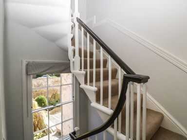 A carpeted staircase with white banisters and a black handrail next to a window with a gray blind at 23 Daniel Street in Bath