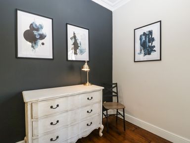 A corner of a room with a white chest of drawers a chair a table lamp three abstract paintings on walls at 23 Daniel Street in Bath