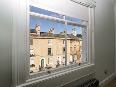 A view of stone townhouses from a window with white trim at 23 Daniel Street in Bath