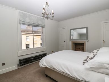 A bedroom with a bed white bedding a window with a blind a radiator and a fireplace with a mirror above at 23 Daniel Street Bath