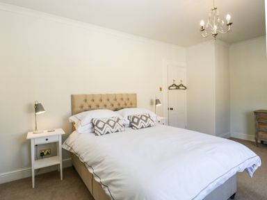 A bedroom with a bed flanked by two bedside tables each with a lamp and a door with hangers on it at 23 Daniel Street in Bath