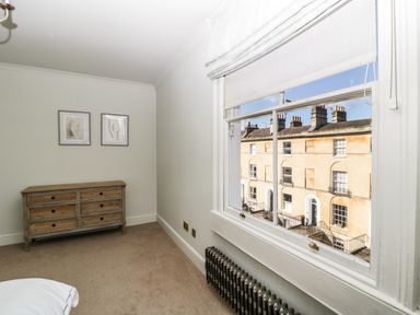 A bedroom with a wooden dresser two framed pictures and a window overlooking buildings at 23 Daniel Street in Bath