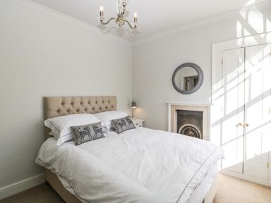A bedroom with a bed white bedding a tufted headboard bedside table lamp fireplace and a round mirror at 23 Daniel Street Bath