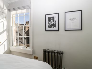 A bedroom window with roman blinds next to framed pictures and a radiator at 23 Daniel Street in Bath
