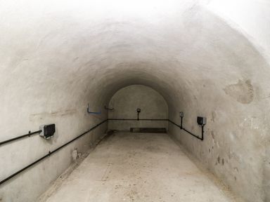 An empty tunnel like room with concrete floor and curved ceiling with mounted electrical components along the walls at 23 Daniel Street in Bath