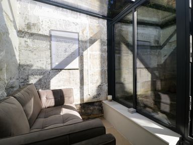 A seating area with a brown sofa a framed picture on a stone wall and large glass windows at 23 Daniel Street in Bath