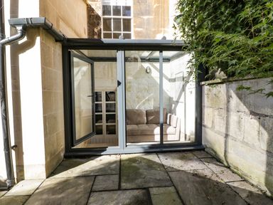 Glass enclosed conservatory with a brown sofa viewed from outside on a stone patio at 23 Daniel Street in Bath