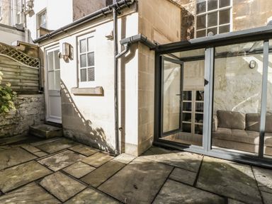A stone patio with a white door and window next to a glass door leading to a room with a sofa at 23 Daniel Street in Bath