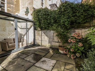 A paved outdoor patio area with potted plants and a glass enclosure containing a sofa at 23 Daniel Street in Bath