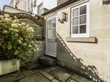 An outdoor area with a white door and window on a stone wall a plant in a pot and a wooden fence at 23 Daniel Street in Bath