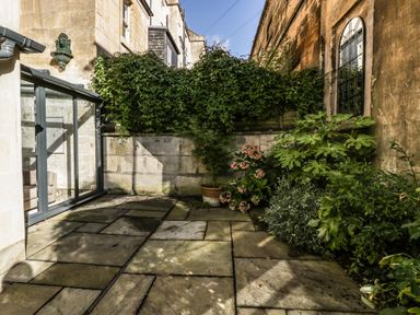 A small paved courtyard with potted and planted greenery and a glass door leading inside at 23 Daniel Street in Bath