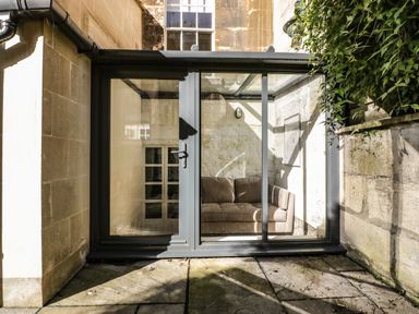 A small enclosed glass porch with a brown sofa inside at 23 Daniel Street in Bath