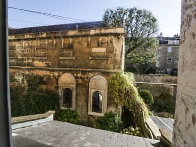 An exterior view of a stone building with arched windows and climbing plants at 23 Daniel Street in Bath