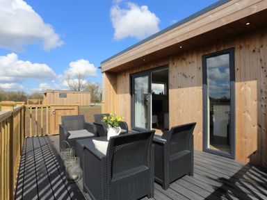 An outdoor wooden deck with black wicker chairs and a table with flowers at The Wren in Wem