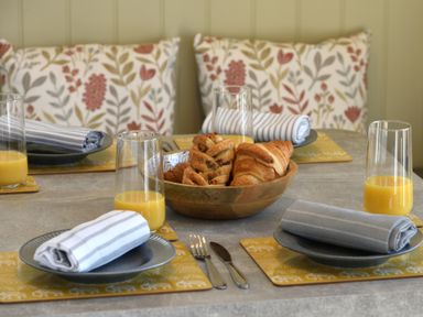 A dining table set with plates napkins glasses of orange juice and a bowl of croissants at The Wren in Wem