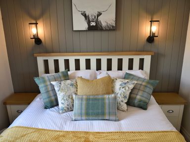 A bed with patterned and plain pillows and a yellow throw blanket between two bedside tables with lamps at The Wren in Wem