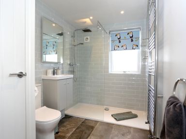 A bathroom with a shower area, toilet, sink, mirror, towel rail, and window with patterned blind at The Wren in Wem