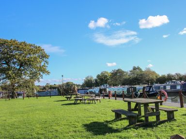 A grassy area with wooden picnic tables near a canal with moored boats at The Wren in Wem