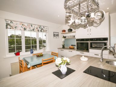 A kitchen with a dining table by the window and hanging pots above a countertop at Creekside House in Fowey