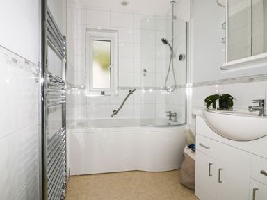 A bathroom with a bathtub shower combination a sink with cabinets and a window at Creekside House in Fowey