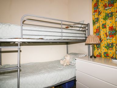 A bedroom with metal bunk beds a teddy bear on the bottom bed a table lamp and colorful curtains at Creekside House in Fowey