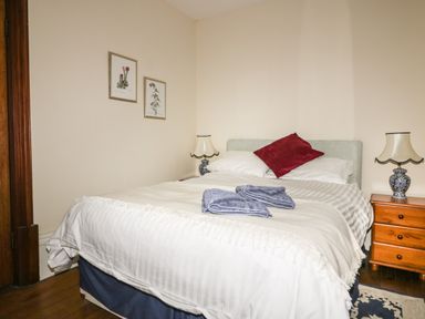 A bedroom with a bed with white bedding two blue towels on the bed a red pillow two bedside tables with lamps and two framed pictures on the wall at Creekside House in Fowey