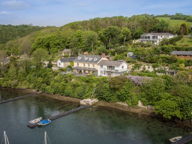 A waterfront house with a dock and boats surrounded by trees and gardens at Creekside House in Fowey