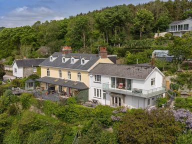 A large multi-section house with outdoor seating on terraces surrounded by trees at Creekside House in Fowey