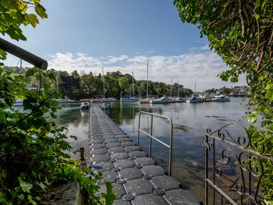 A floating dock leading to moored boats on a river with trees in the background at Creekside House in Fowey
