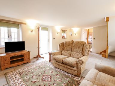 A living room with patterned sofas a wooden TV stand a flat screen TV and a patterned rug at Postbox Cottage in Feltwell
