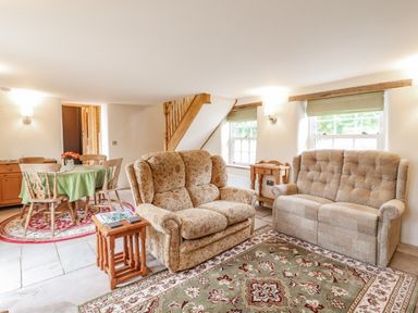 A living room with two sofas and a small wooden side table next to a dining area with a round table and four chairs at Postbox Cottage in Feltwell