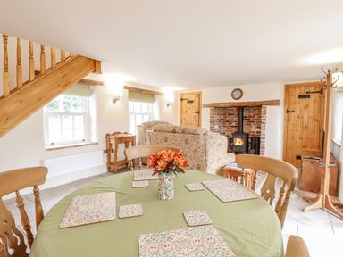 A living room with a table with a green tablecloth and flowers and a fireplace with chairs at Postbox Cottage in Feltwell