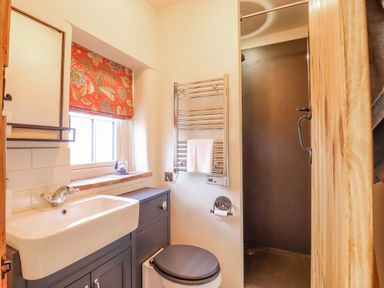 A bathroom with a sink vanity unit toilet shower and a window with floral curtain at Postbox Cottage in Feltwell