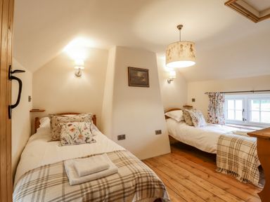 A bedroom with two single beds wooden floor and a window with floral curtains at Postbox Cottage in Feltwell