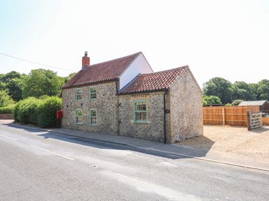 A traditional stone cottage with green windows by a road and a gravel driveway at Postbox Cottage in Feltwell