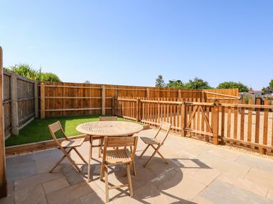 An outdoor patio area with a round wooden table and four wooden chairs fenced garden at Postbox Cottage in Feltwell