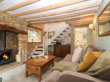 A living room with a sofa and wooden coffee table near a fireplace and a staircase at Tuesday Cottage in Bourton-On-The-Water