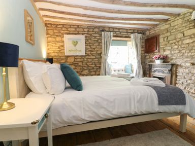 A bedroom with a bed white bedside table blue lamps and a window seat at Tuesday Cottage in Bourton-On-The-Water