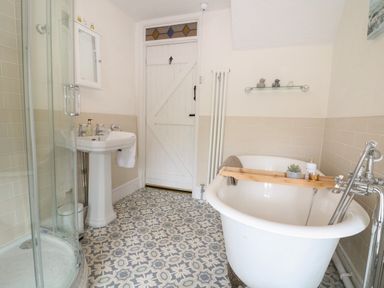 A bathroom with a clawfoot bathtub a patterned tile floor a white sink and a glass enclosed shower at Tuesday Cottage in Bourton-On-The-Water