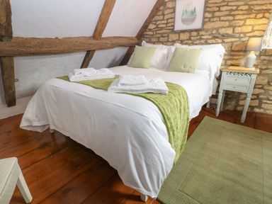 A bedroom with a double bed white and green bedding wooden floor side table with lamp and exposed wooden beams at Tuesday Cottage in Bourton-On-The-Water