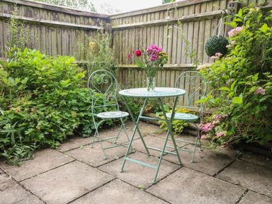 A small garden patio with two metal chairs and a round metal table with flowers on it at Tuesday Cottage in Bourton-On-The-Water