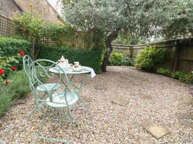 An outdoor patio area with two light green metal chairs and a table with tea set surrounded by plants at Tuesday Cottage in Bourton-On-The-Water