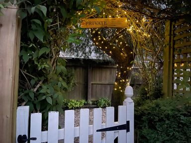 A garden gate with a private sign and fairy lights wrapped around a tree at Tuesday Cottage in Bourton-On-The-Water