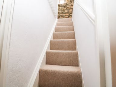 A narrow carpeted staircase with white walls and a stone wall at the top at Tuesday Cottage in Bourton-On-The-Water