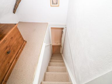 A carpeted staircase leading down from an upper floor with white walls and a wooden chest at Tuesday Cottage in Bourton-On-The-Water