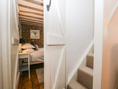 A narrow hallway with carpeted stairs and a white door leading to a bedroom with a bed and nightstand at Tuesday Cottage in Bourton-On-The-Water