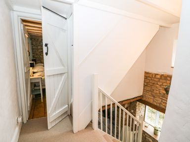 A staircase with white railing leading down and a partially open white wooden door revealing a bedroom at Tuesday Cottage in Bourton-On-The-Water