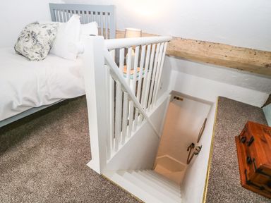 A carpeted loft bedroom with a bed pillows lamp wooden chest and staircase leading down at Tuesday Cottage in Bourton-On-The-Water