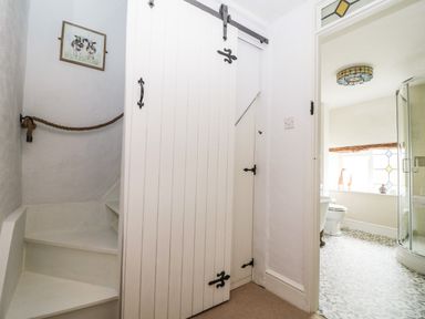 A white stairway with a rope handrail a sliding barn door and a bathroom with a glass shower and patterned floor tiles at Tuesday Cottage in Bourton-On-The-Water